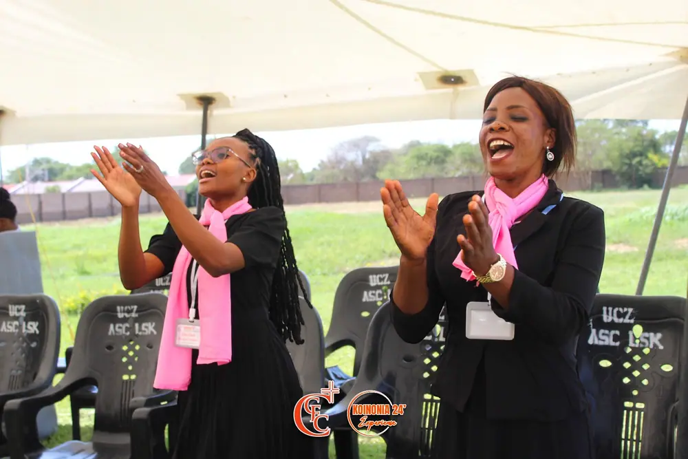Two women in pink scarves clapping and singing in worship